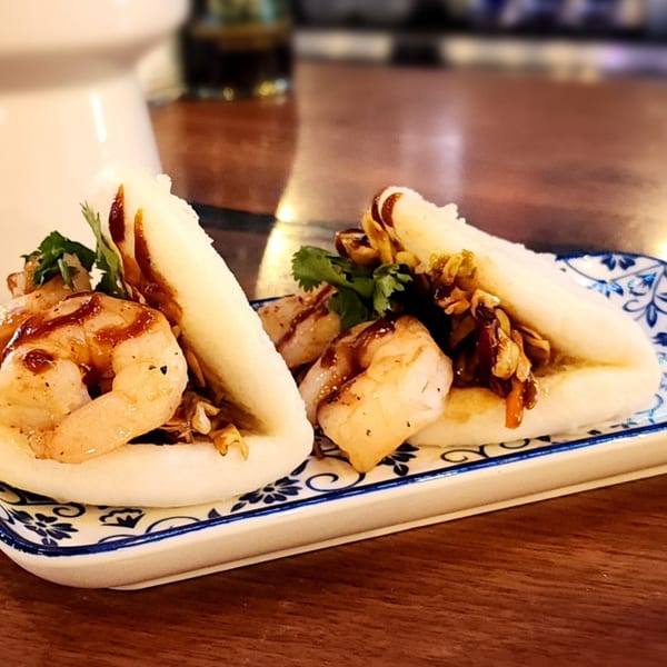 Two bao buns filled with shrimp, scallops, and sauce on a patterned plate.