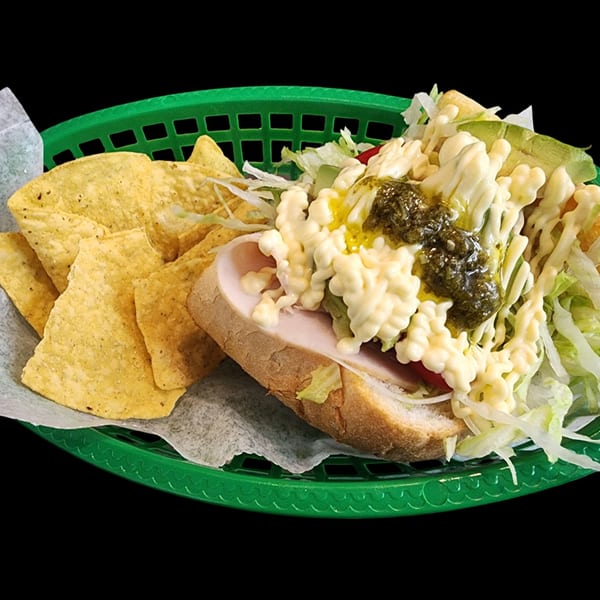 A sandwich with turkey, lettuce, tomato, avocado, mayonnaise, and pesto, served with tortilla chips.