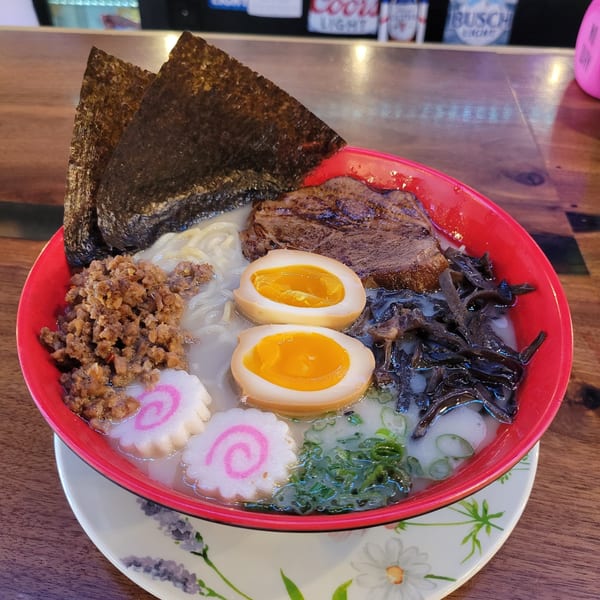 A vibrant red bowl of ramen with pork, eggs, seaweed, fish cakes, and green onions.