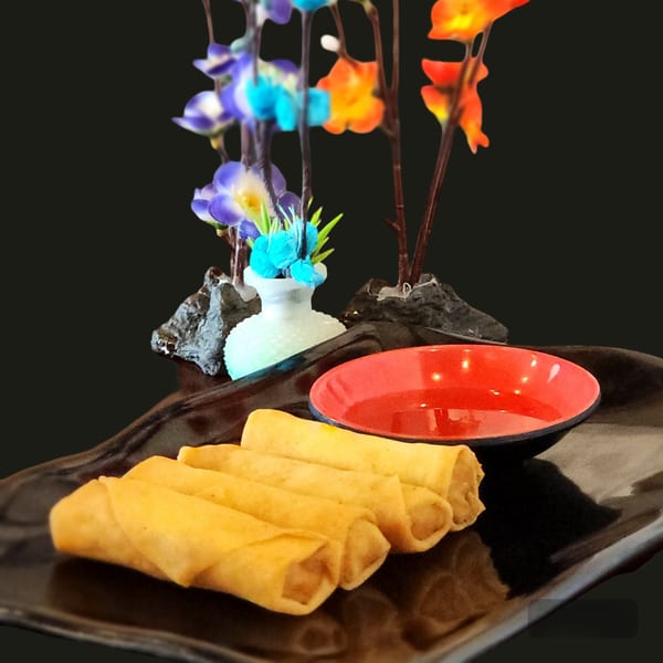 Golden spring rolls with a red dipping sauce and decorative flowers on a black plate.