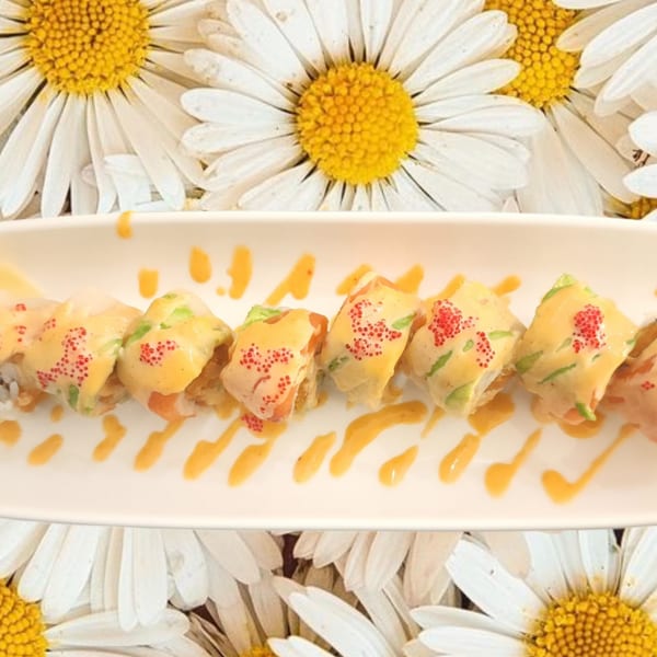 Sushi rolls with orange sauce and red roe on a white plate, against a background of daisies.