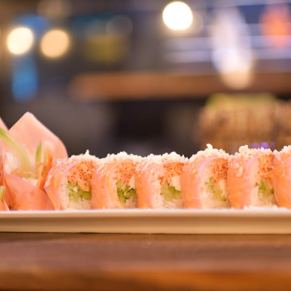 Close-up of a sushi roll with salmon, cucumber, and rice, topped with crunchy flakes.