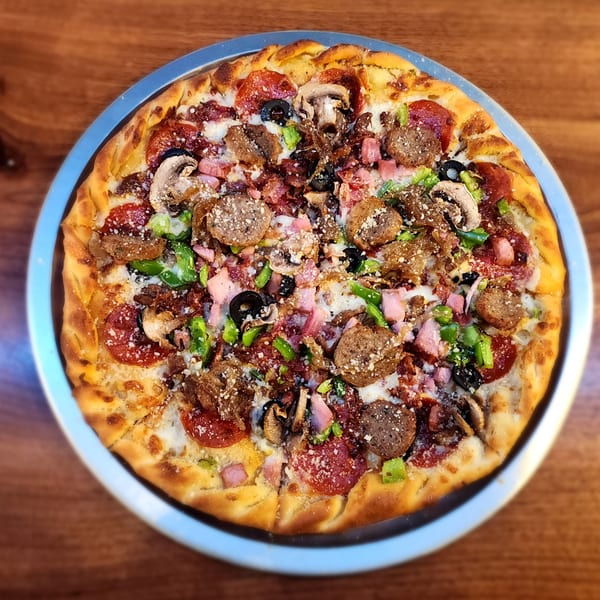 A whole pizza with pepperoni, sausage, mushrooms, olives, and green peppers on a metal tray.