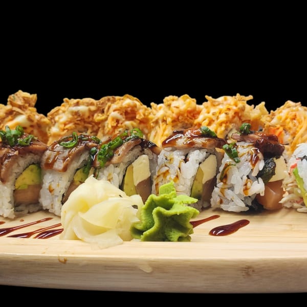 Sushi rolls with eel, avocado, and crispy toppings, served with ginger and wasabi on a wooden board.