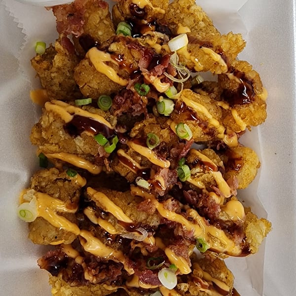 Crispy tater tots drizzled with orange sauce, dark glaze, bacon bits, and green onions.